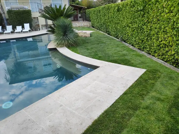 Pelouse entretenue entre une haie et les abords d’une piscine