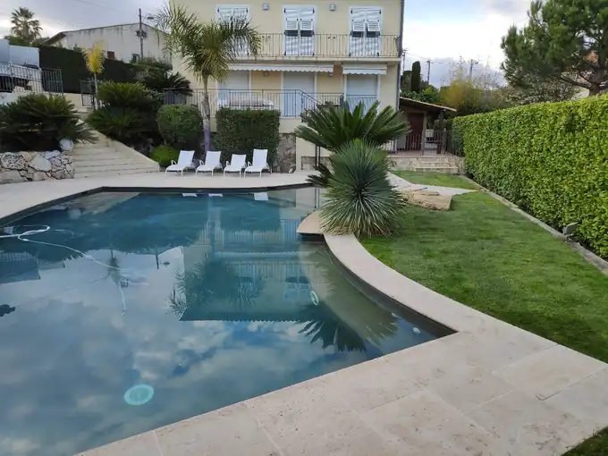 Jardin de villa avec pelouse, haies taillées et palmiers autour d’une piscine